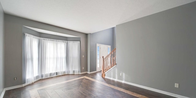 empty room featuring a textured ceiling, parquet floors, stairway, and baseboards