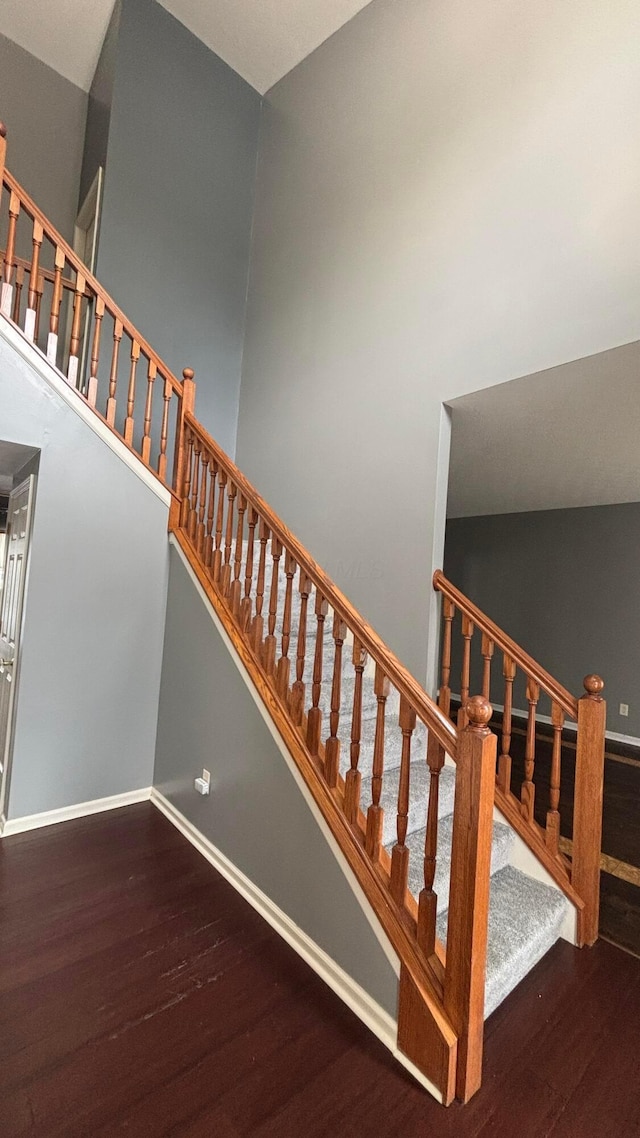 stairway with a high ceiling, baseboards, and wood finished floors