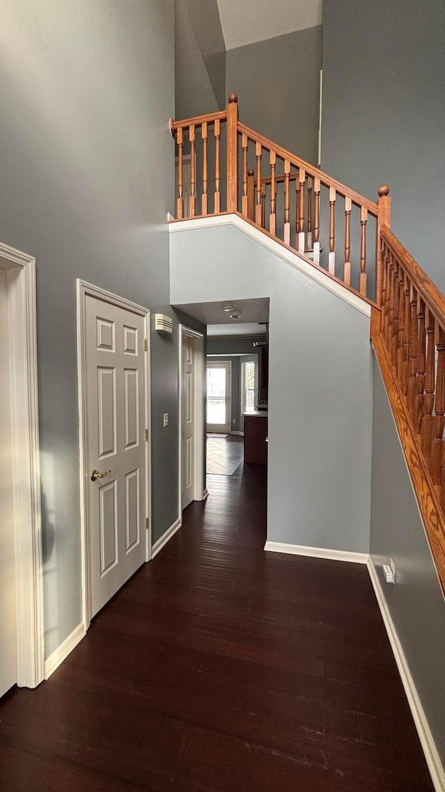 hallway with a high ceiling, stairs, baseboards, and wood finished floors