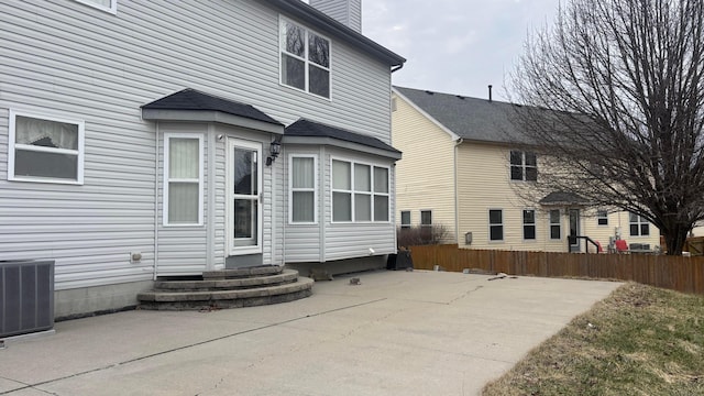 rear view of house with entry steps, central AC, fence, a chimney, and a patio area