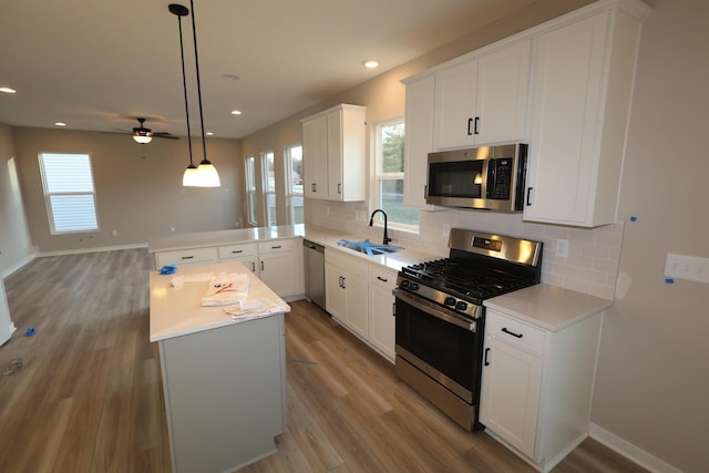 kitchen with light wood finished floors, tasteful backsplash, light countertops, appliances with stainless steel finishes, and a sink