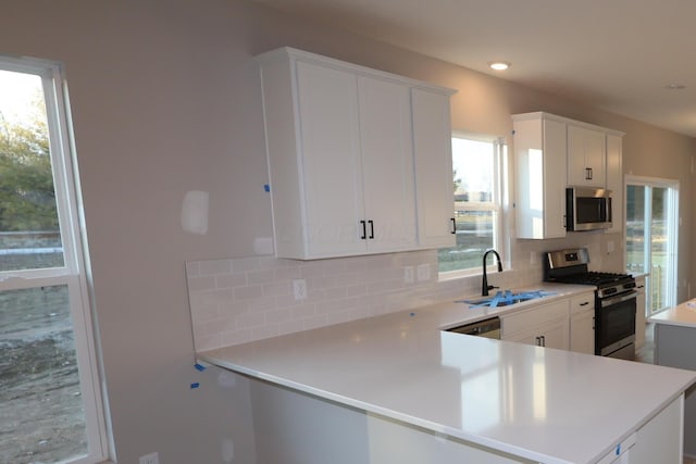 kitchen with appliances with stainless steel finishes, a sink, light countertops, white cabinetry, and backsplash