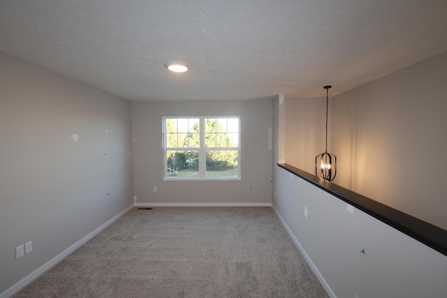 spare room with light carpet, a textured ceiling, visible vents, and baseboards