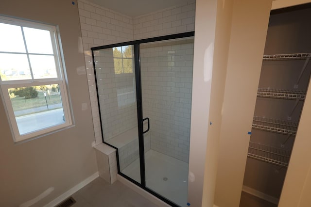 bathroom with a walk in closet, a shower stall, and baseboards