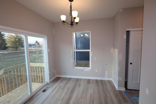 unfurnished dining area with a notable chandelier, baseboards, visible vents, and wood finished floors