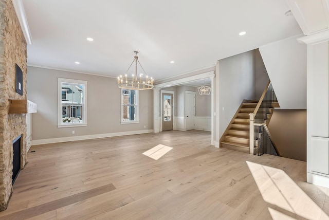 unfurnished living room featuring light wood-type flooring, a fireplace, crown molding, and a chandelier