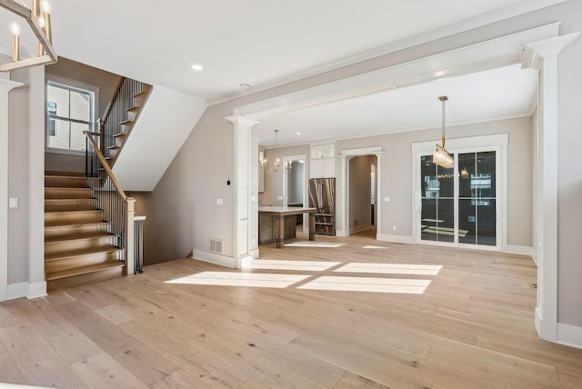 unfurnished living room with light wood-type flooring, ornamental molding, and an inviting chandelier