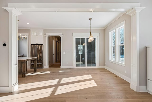 unfurnished dining area featuring decorative columns, ornamental molding, a notable chandelier, and light wood-type flooring