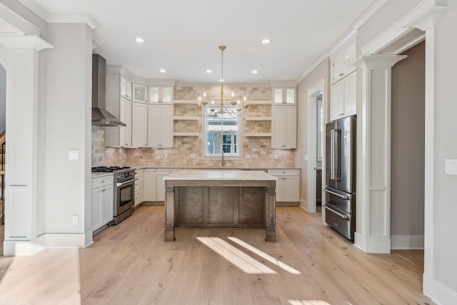 kitchen with premium appliances, white cabinets, decorative light fixtures, wall chimney range hood, and sink