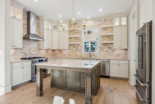 kitchen featuring decorative light fixtures, wall chimney range hood, a kitchen island, sink, and premium appliances