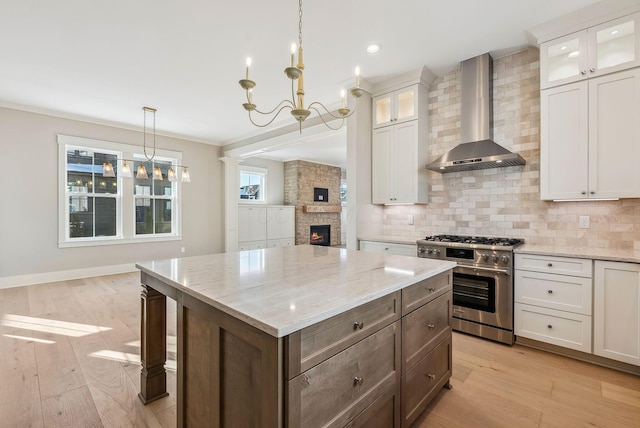 kitchen with decorative light fixtures, stainless steel stove, decorative backsplash, white cabinets, and wall chimney exhaust hood