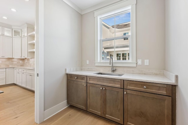 bar with decorative backsplash, light hardwood / wood-style flooring, white cabinets, and sink