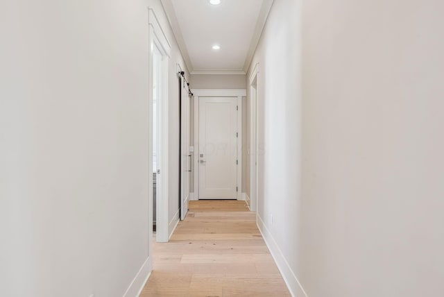 corridor featuring light hardwood / wood-style floors, ornamental molding, and a barn door