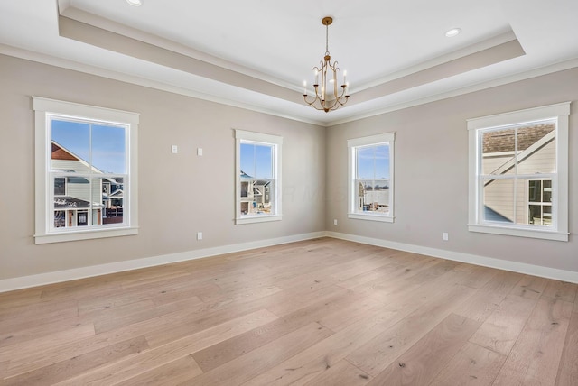 empty room featuring a tray ceiling, light hardwood / wood-style flooring, crown molding, and a chandelier