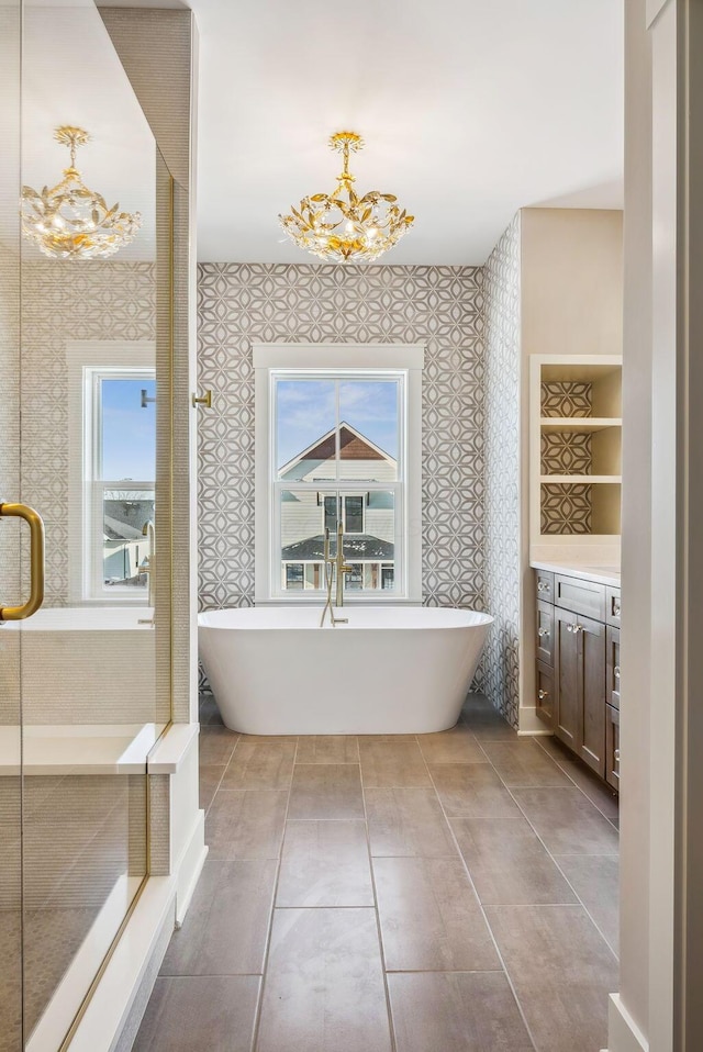 bathroom with a chandelier, a healthy amount of sunlight, a tub to relax in, and vanity