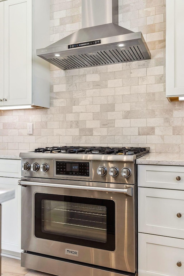 kitchen with white cabinets, gas stove, decorative backsplash, light stone counters, and range hood