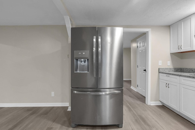 kitchen with light stone countertops, a textured ceiling, light hardwood / wood-style flooring, stainless steel fridge with ice dispenser, and white cabinetry