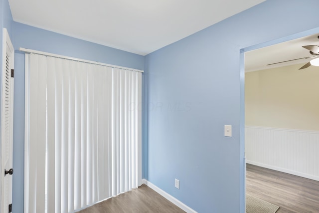 unfurnished room with ceiling fan, wood finished floors, and wainscoting