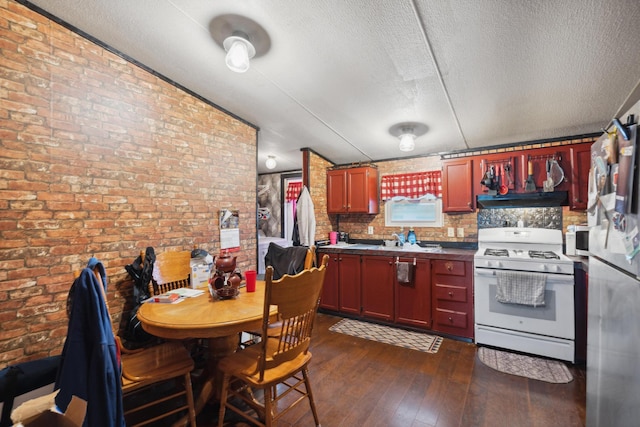 kitchen with stainless steel refrigerator, gas range gas stove, dark wood-type flooring, brick wall, and exhaust hood