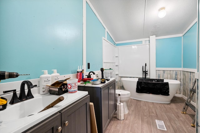 bathroom with hardwood / wood-style floors, lofted ceiling, a textured ceiling, a bathtub, and vanity