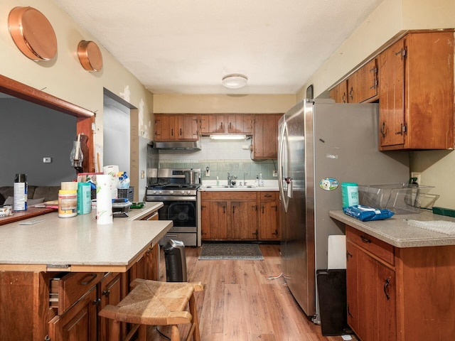 kitchen featuring kitchen peninsula, a kitchen breakfast bar, stainless steel appliances, sink, and light hardwood / wood-style flooring