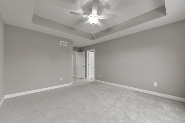 spare room featuring ceiling fan, light colored carpet, and a tray ceiling