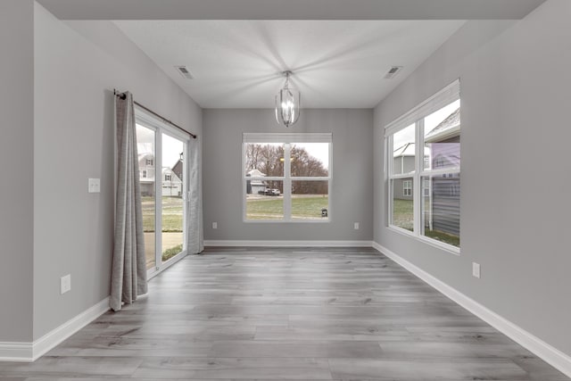 unfurnished dining area with a wealth of natural light, a notable chandelier, and light wood-type flooring