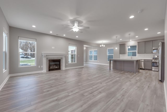 unfurnished living room featuring light wood-type flooring and ceiling fan with notable chandelier