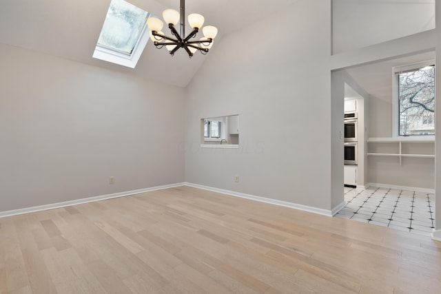 interior space featuring a chandelier, a skylight, high vaulted ceiling, and light hardwood / wood-style flooring