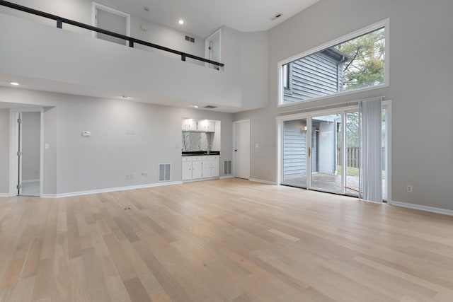 unfurnished living room with a high ceiling and light hardwood / wood-style floors