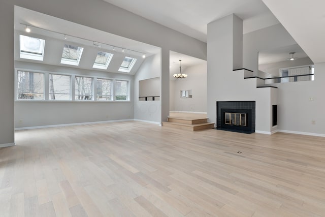 unfurnished living room with light hardwood / wood-style flooring, rail lighting, high vaulted ceiling, and an inviting chandelier