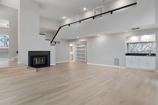 unfurnished living room featuring a high ceiling, light wood-type flooring, and sink