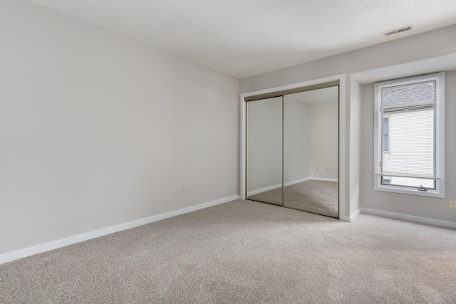 unfurnished bedroom with light colored carpet, a textured ceiling, and a closet