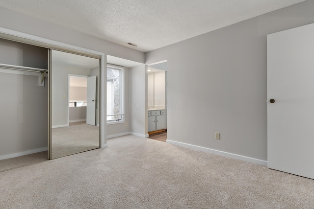 unfurnished bedroom featuring light carpet, a textured ceiling, connected bathroom, and a closet