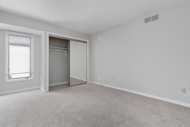 unfurnished bedroom with light carpet, a closet, and a textured ceiling