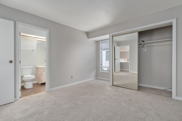 unfurnished bedroom with ensuite bath, light carpet, a closet, and a textured ceiling