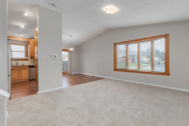 unfurnished living room featuring a textured ceiling, a healthy amount of sunlight, lofted ceiling, and light carpet