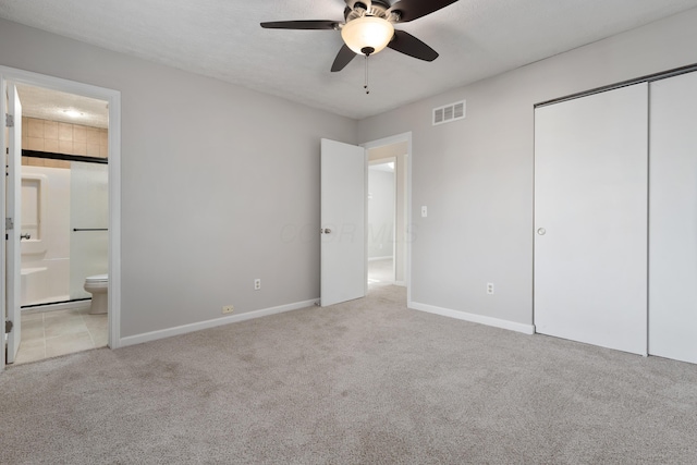 unfurnished bedroom featuring ceiling fan, light colored carpet, ensuite bath, and a closet