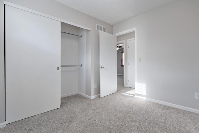 unfurnished bedroom featuring light colored carpet, a textured ceiling, and a closet