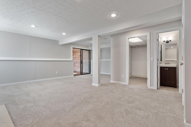 basement featuring sink, light colored carpet, and a textured ceiling