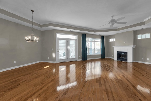 unfurnished living room featuring crown molding, hardwood / wood-style flooring, a tray ceiling, a tiled fireplace, and ceiling fan with notable chandelier