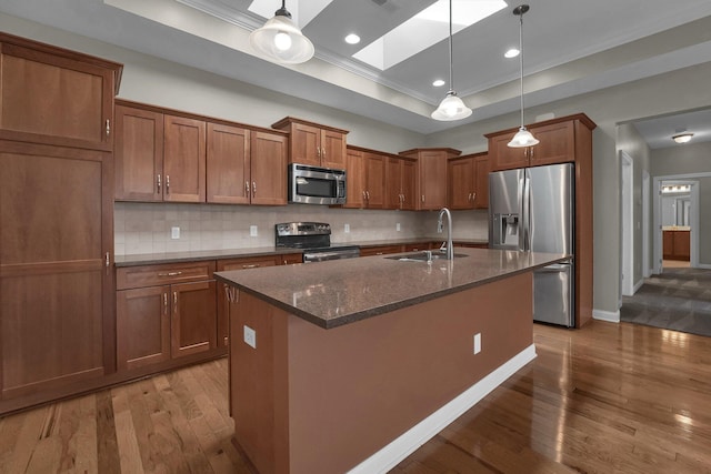 kitchen with sink, hanging light fixtures, a raised ceiling, an island with sink, and stainless steel appliances