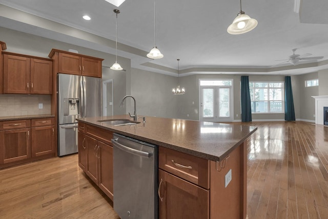 kitchen with sink, light hardwood / wood-style flooring, appliances with stainless steel finishes, a center island with sink, and decorative light fixtures