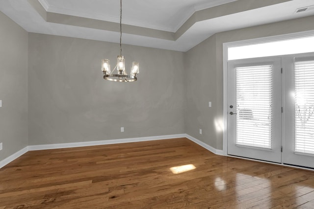 unfurnished dining area featuring crown molding, wood-type flooring, a raised ceiling, and a notable chandelier