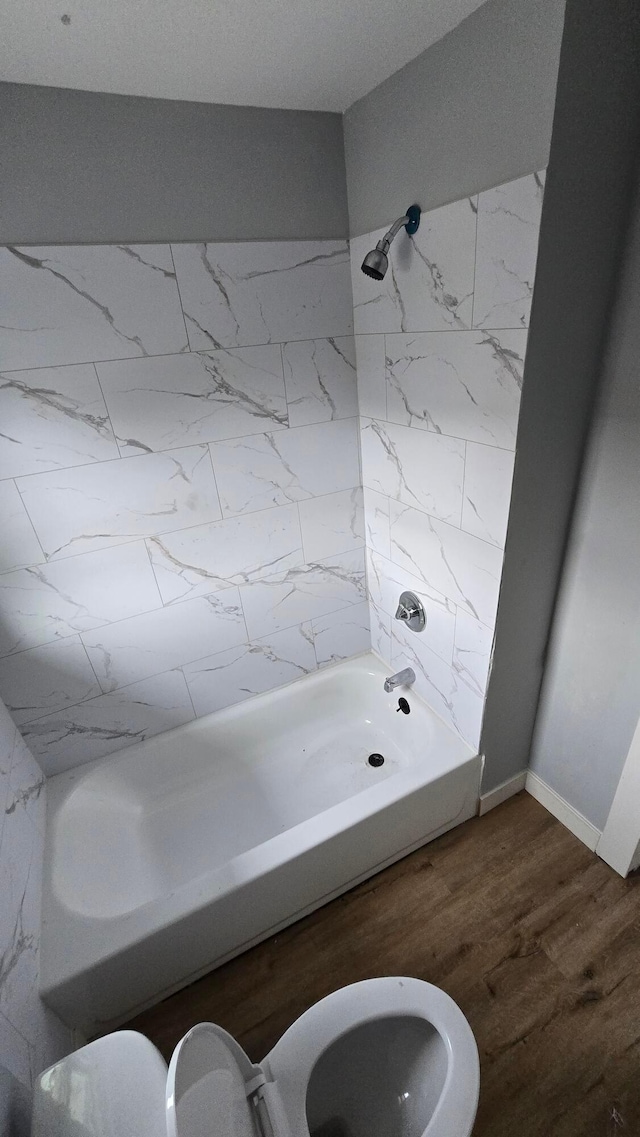 bathroom with tiled shower / bath combo, hardwood / wood-style flooring, and toilet