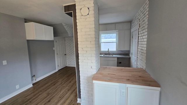 kitchen with wooden counters, brick wall, dark wood-type flooring, sink, and white cabinetry