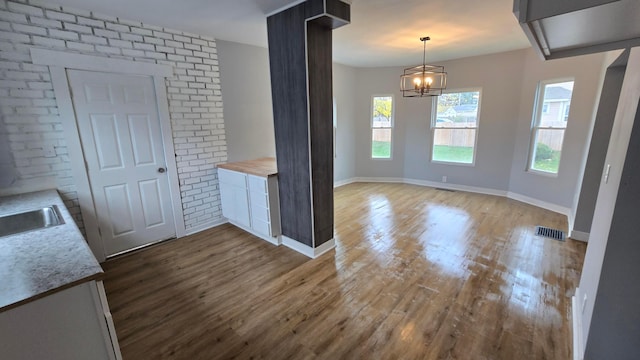 unfurnished dining area with hardwood / wood-style floors, sink, a notable chandelier, and brick wall