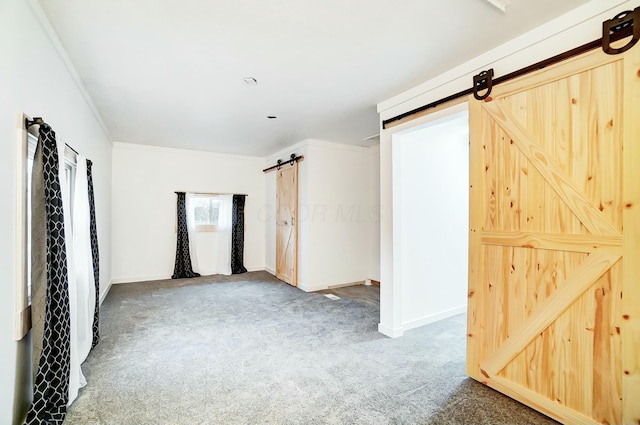 empty room featuring carpet, a barn door, and crown molding