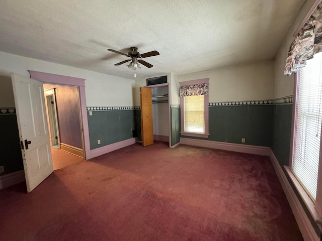 unfurnished bedroom featuring carpet flooring, a textured ceiling, multiple windows, and ceiling fan