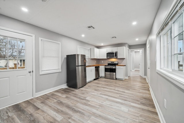 kitchen with white cabinets, wood counters, stainless steel appliances, and light hardwood / wood-style flooring